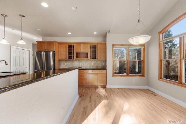 kitchen with light wood-type flooring, freestanding refrigerator, glass insert cabinets, dark countertops, and tasteful backsplash