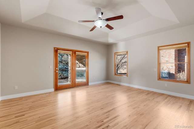 empty room featuring light wood-type flooring, a raised ceiling, and baseboards