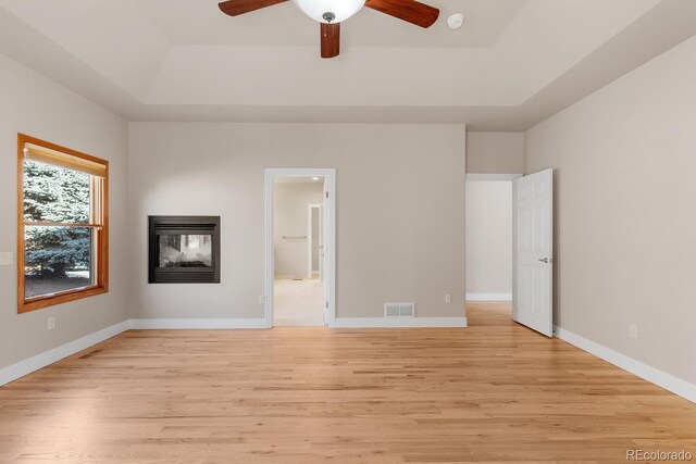 unfurnished bedroom with a multi sided fireplace, visible vents, light wood-type flooring, and a raised ceiling