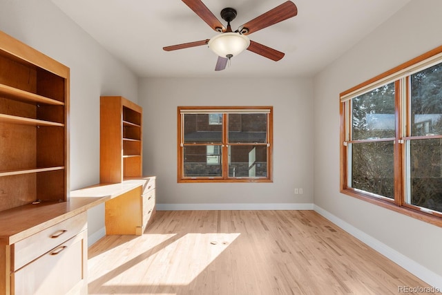 unfurnished office with built in study area, light wood-type flooring, baseboards, and a ceiling fan