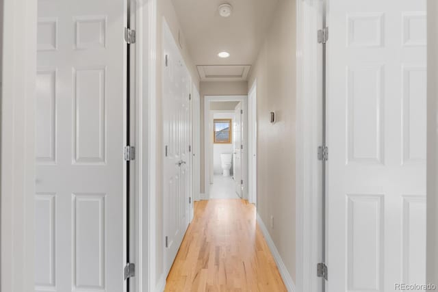 hallway featuring attic access, light wood-style floors, and baseboards