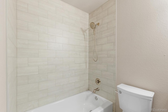 bathroom with toilet, shower / washtub combination, and a textured wall