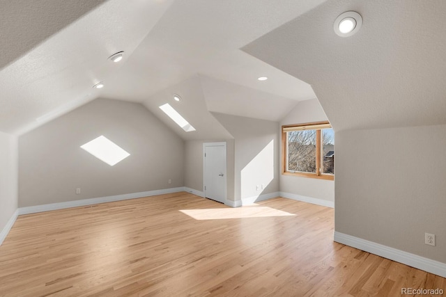 additional living space with light wood finished floors, lofted ceiling with skylight, a textured ceiling, and baseboards