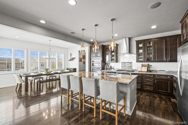 11046 Pastel Pt, Parker, CO 80134 - kitchen featuring wall chimney exhaust hood, stainless steel appliances, dark brown cabinets, tasteful backsplash, and glass insert cabinets