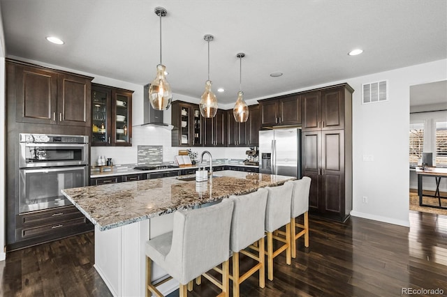 11046 Pastel Pt, Parker, CO 80134 - kitchen with appliances with stainless steel finishes, a sink, dark brown cabinets, a breakfast bar, and light stone countertops