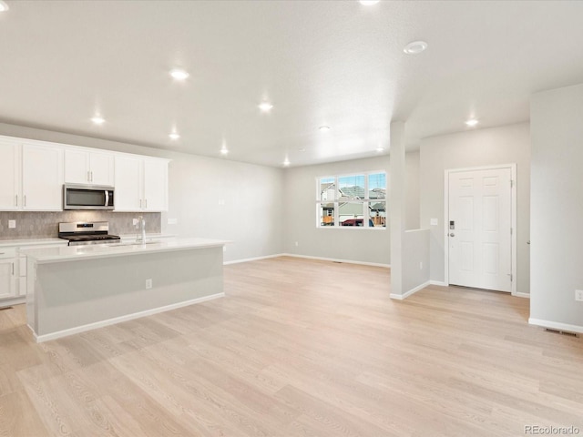 kitchen featuring a kitchen island with sink, white cabinets, light hardwood / wood-style flooring, tasteful backsplash, and stainless steel appliances