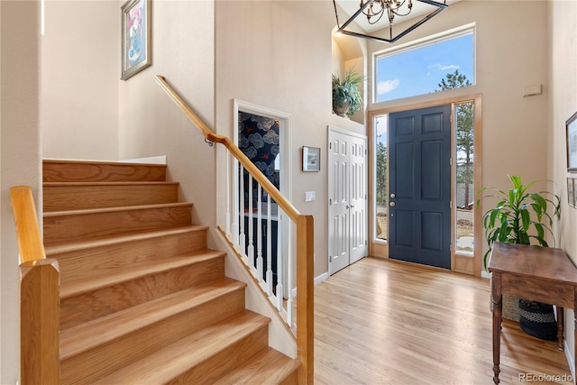 entrance foyer featuring stairway, a towering ceiling, an inviting chandelier, wood finished floors, and baseboards