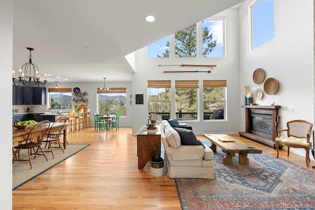 living room with a chandelier, recessed lighting, baseboards, light wood-style floors, and a glass covered fireplace