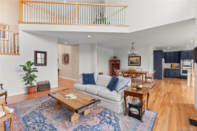 living room featuring baseboards, a towering ceiling, light wood-style floors, a notable chandelier, and recessed lighting