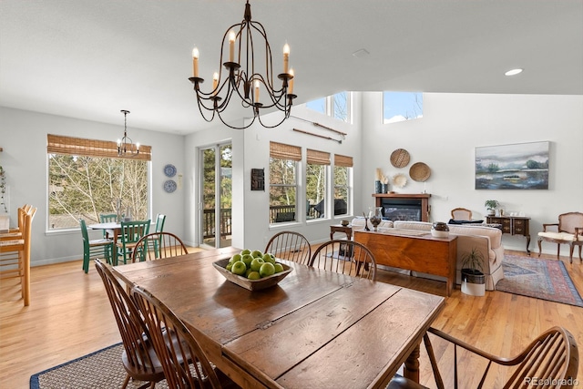 dining area with light wood-style flooring, a chandelier, baseboards, and a glass covered fireplace