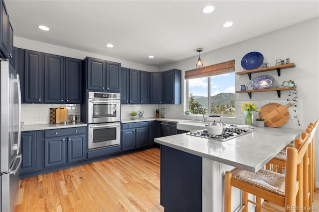 kitchen with stainless steel appliances, a sink, blue cabinets, light wood-type flooring, and a peninsula