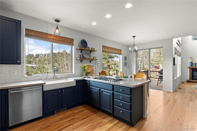 kitchen with decorative backsplash, a peninsula, stainless steel appliances, blue cabinetry, and a sink