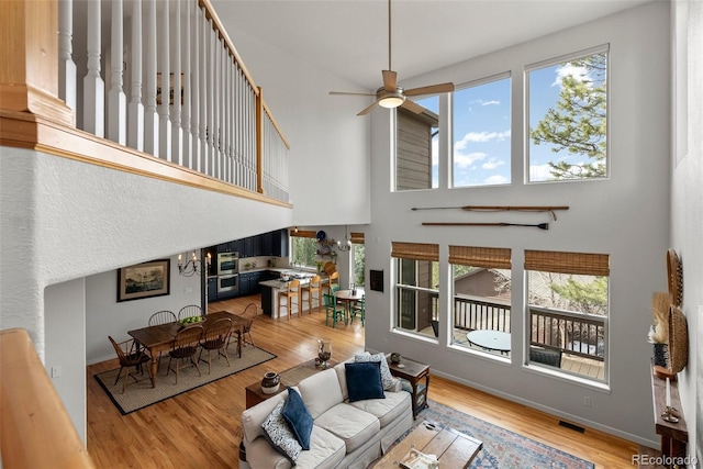 living room with ceiling fan, a high ceiling, wood finished floors, visible vents, and baseboards