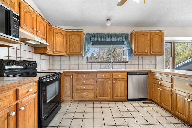 kitchen with a textured ceiling, under cabinet range hood, tile counters, electric range, and stainless steel dishwasher