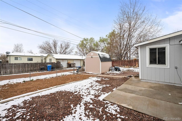 snowy yard featuring a storage unit, a fenced backyard, an outbuilding, and a patio