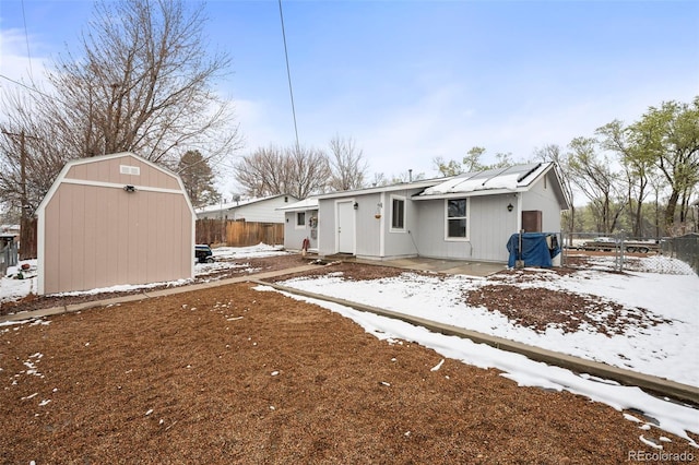 snow covered rear of property featuring fence, an outbuilding, a shed, and a patio