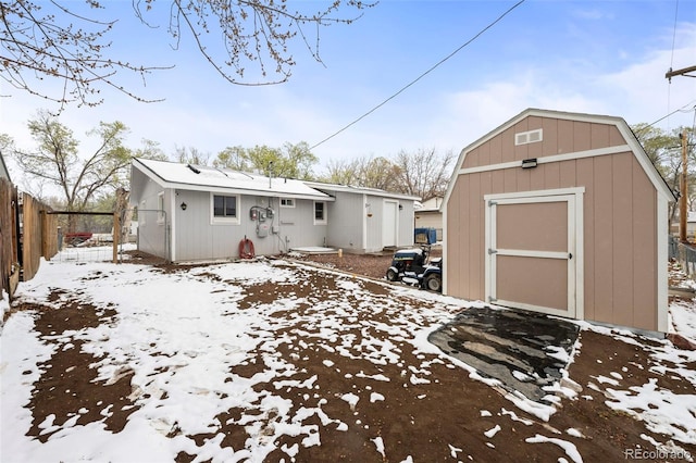 snow covered back of property with an outdoor structure, a shed, and fence