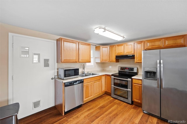 kitchen featuring appliances with stainless steel finishes, a sink, light countertops, light wood-type flooring, and under cabinet range hood
