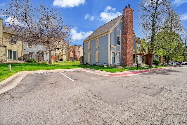 view of property exterior featuring board and batten siding, a chimney, a lawn, a residential view, and uncovered parking