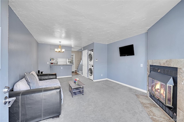 carpeted living area featuring stacked washer and dryer, baseboards, a textured ceiling, a chandelier, and a fireplace with flush hearth