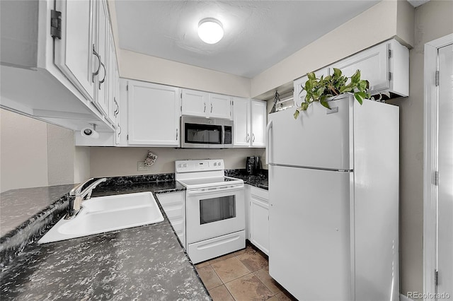 kitchen featuring dark countertops, a sink, light tile patterned floors, white appliances, and white cabinetry