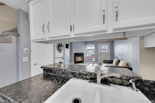 kitchen featuring stacked washer and clothes dryer, a glass covered fireplace, open floor plan, white cabinetry, and a sink