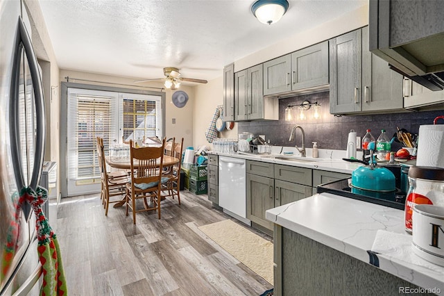 kitchen featuring tasteful backsplash, gray cabinets, freestanding refrigerator, white dishwasher, and light wood-type flooring