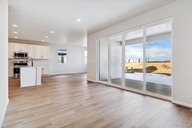 kitchen featuring sink, stainless steel appliances, light hardwood / wood-style flooring, a center island with sink, and white cabinets