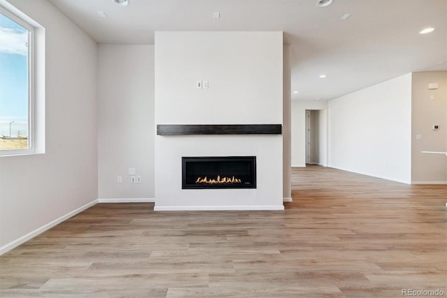 unfurnished living room featuring light wood-style floors, recessed lighting, baseboards, and a glass covered fireplace