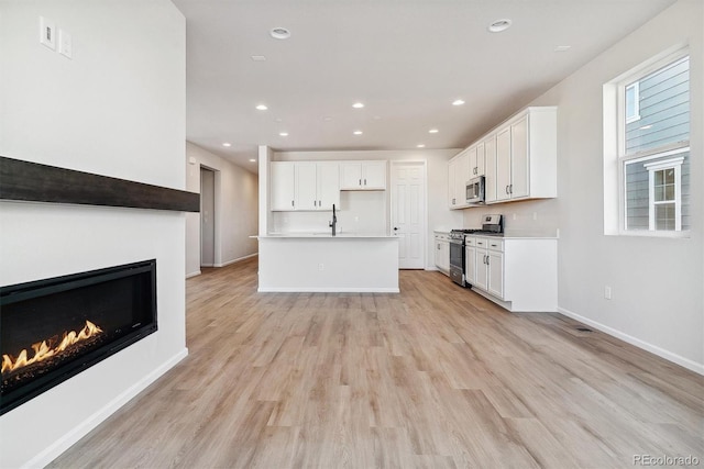 kitchen featuring a center island with sink, white cabinets, light hardwood / wood-style flooring, and appliances with stainless steel finishes