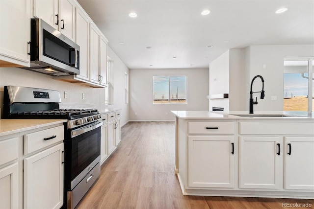 kitchen with backsplash, stainless steel appliances, sink, light hardwood / wood-style flooring, and white cabinets