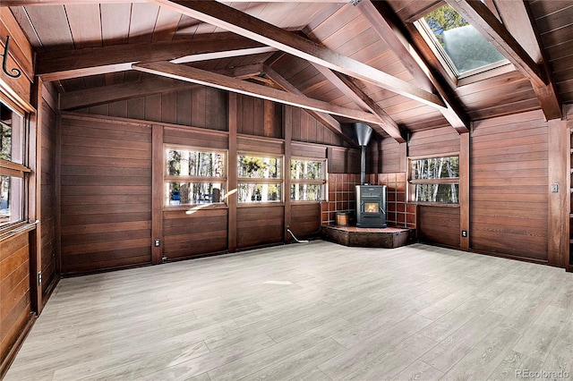 interior space featuring lofted ceiling with skylight, wooden walls, light hardwood / wood-style flooring, wooden ceiling, and a wood stove