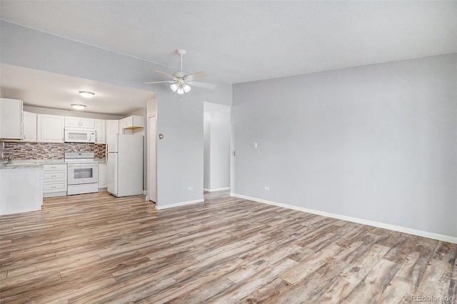 interior space with white appliances, light wood-type flooring, ceiling fan, white cabinetry, and backsplash