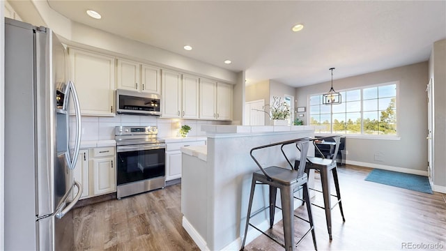 kitchen featuring white cabinetry, light countertops, appliances with stainless steel finishes, hanging light fixtures, and decorative backsplash