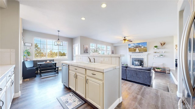 kitchen featuring tile countertops, open floor plan, stainless steel appliances, pendant lighting, and a sink