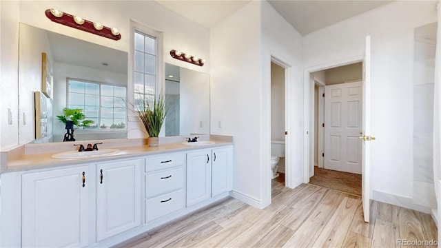 full bath featuring double vanity, a sink, toilet, and wood finished floors