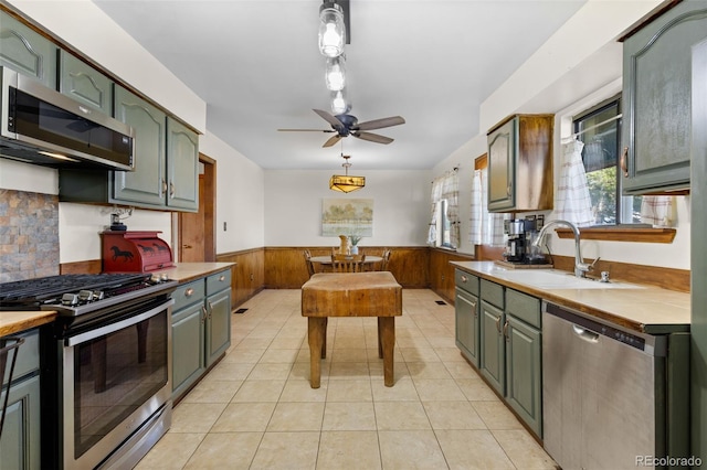 kitchen featuring ceiling fan, sink, stainless steel appliances, wood walls, and light tile patterned floors