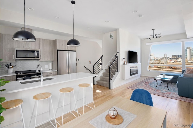 kitchen featuring a breakfast bar area, open floor plan, light countertops, appliances with stainless steel finishes, and a glass covered fireplace