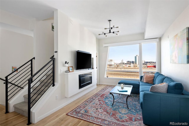 living room with a chandelier, wood finished floors, baseboards, stairway, and a glass covered fireplace