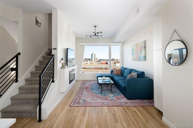 living area with a chandelier, visible vents, baseboards, stairs, and light wood-type flooring