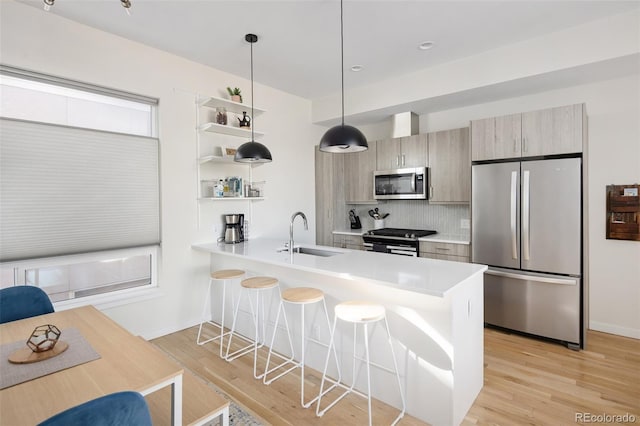 kitchen featuring a peninsula, a breakfast bar, a sink, appliances with stainless steel finishes, and open shelves