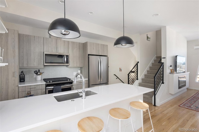 kitchen featuring stainless steel appliances, a sink, light wood-style floors, a kitchen breakfast bar, and modern cabinets