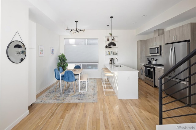 kitchen with light countertops, appliances with stainless steel finishes, light wood-style floors, a sink, and a kitchen breakfast bar