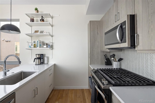 kitchen with light wood-style flooring, a sink, light countertops, appliances with stainless steel finishes, and tasteful backsplash