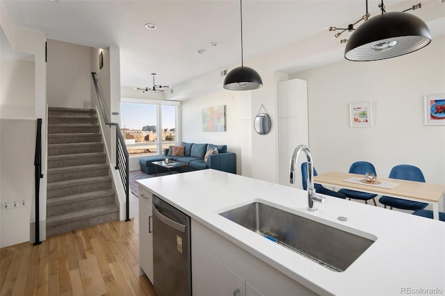 kitchen featuring decorative light fixtures, light countertops, stainless steel dishwasher, light wood-style floors, and a sink