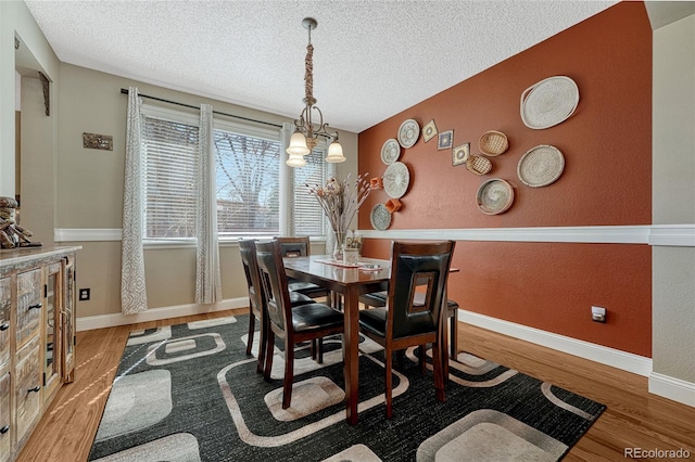 dining space with a notable chandelier, a textured ceiling, baseboards, and wood finished floors