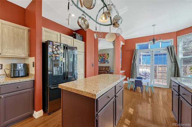 kitchen featuring light wood finished floors, backsplash, a kitchen island, light countertops, and black refrigerator with ice dispenser