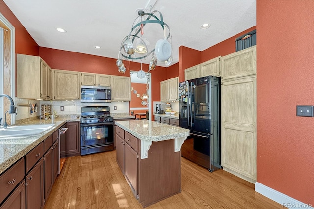 kitchen with a sink, light wood-type flooring, black appliances, and a center island