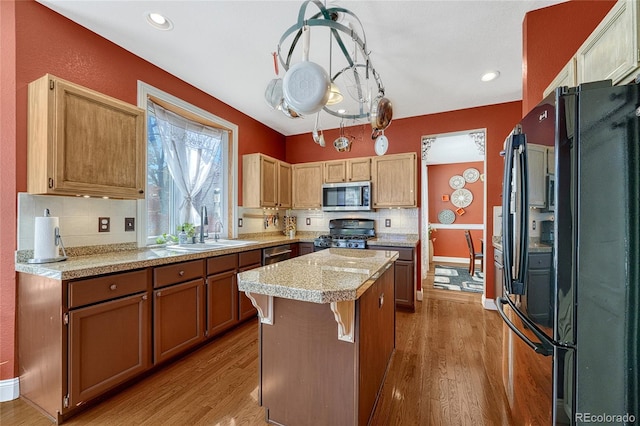 kitchen with a sink, a kitchen island, wood finished floors, stainless steel appliances, and decorative backsplash