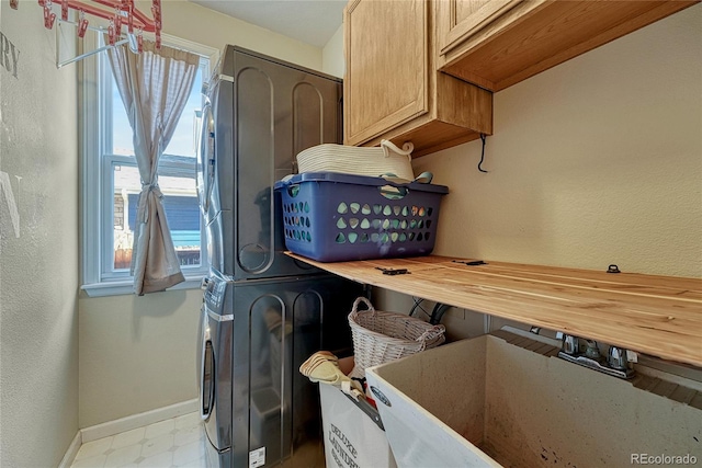 laundry area featuring baseboards, stacked washer and clothes dryer, tile patterned floors, cabinet space, and a sink